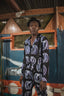 Chic Accra Jumpsuit with Good Signal batik design, long sleeves, and waist belt, set against blue-painted interior.