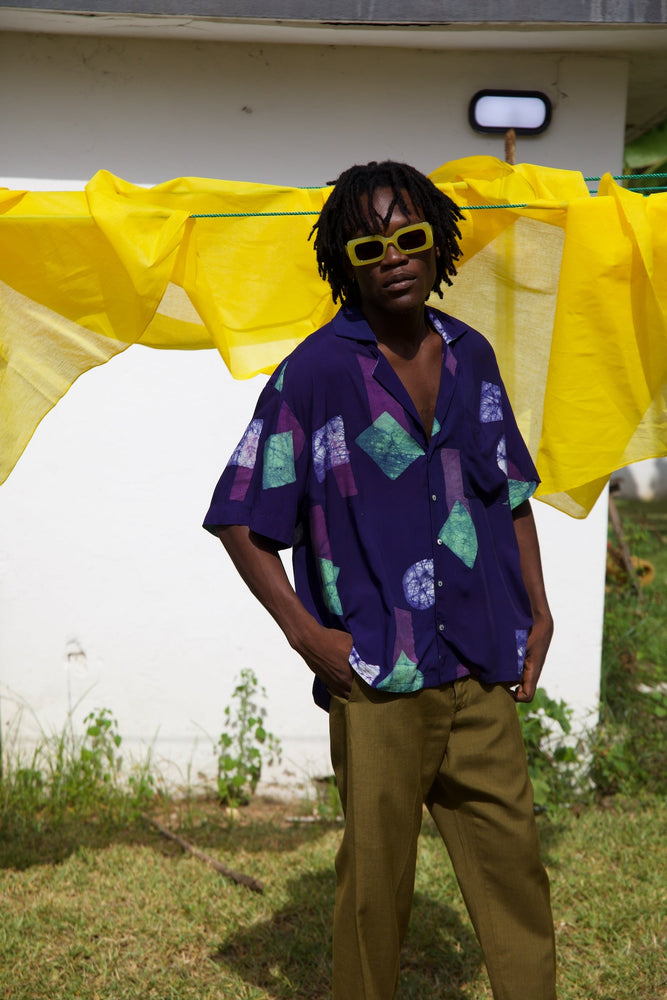 A man in a relaxed pose in the dark purple and colorful geometric shapes print rayon Holiday shirt.