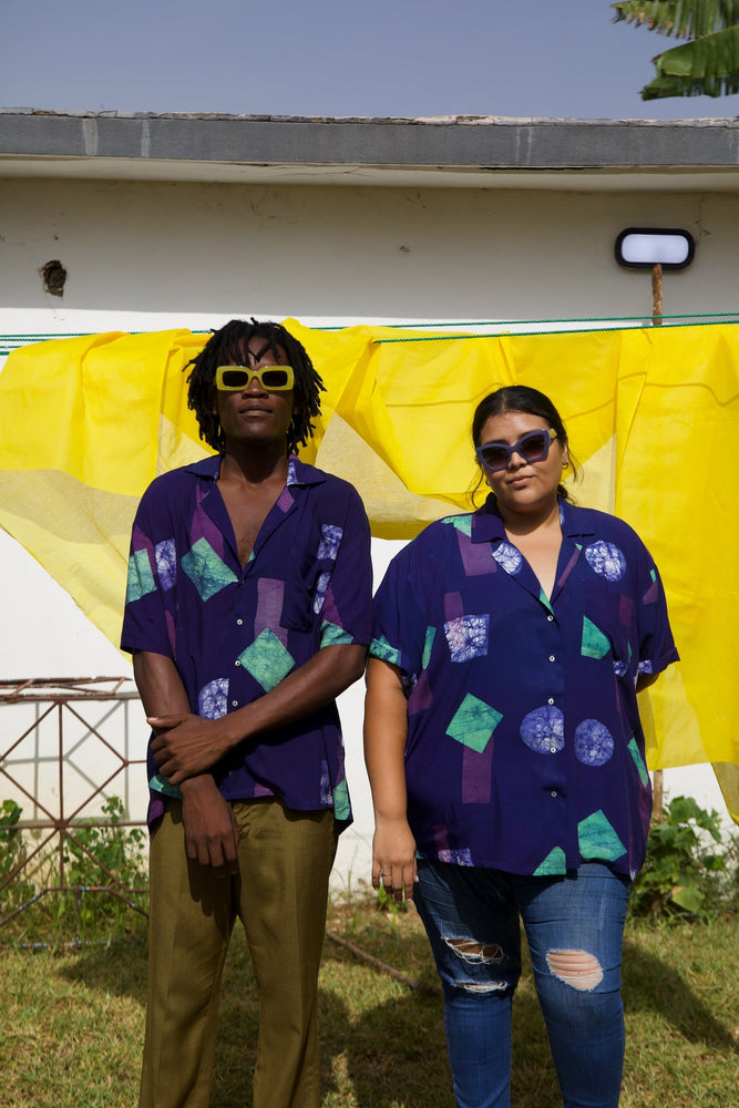 A woman and a man wearing the rayon Holiday Shirt in dark purple and geometric shapes print, showcasing its versatility.