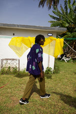 A person wearing a vibrant purple rayon holiday shirt with green and white abstract patterns, walking outdoors.