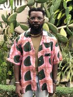 A man wearing the same rayon shirt unbuttoned, standing in front of lush flora.