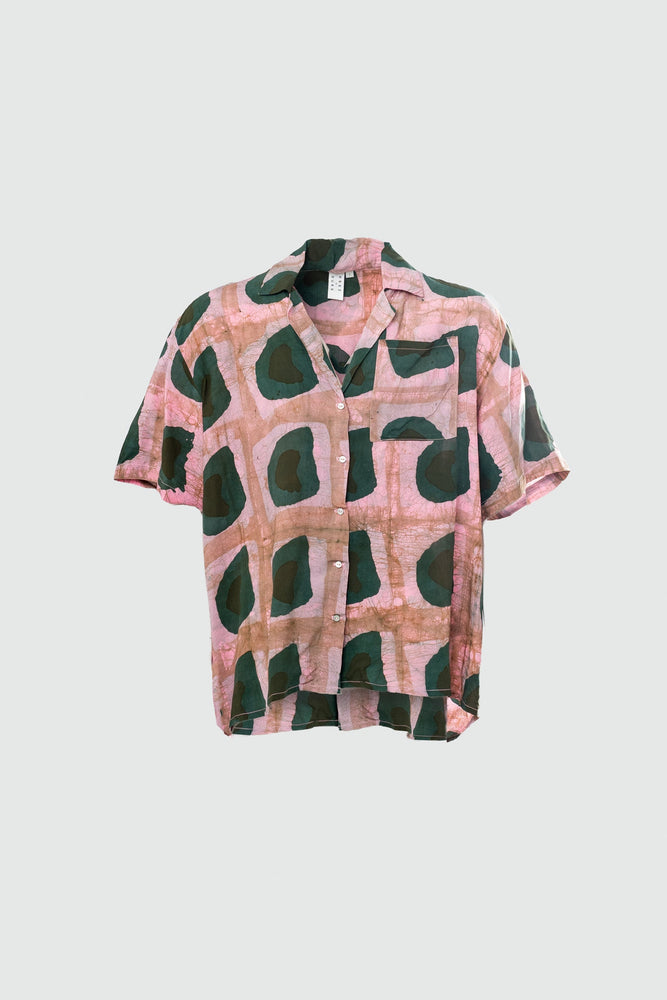 A front view ghost mannequin image of the same shirt, batiked pink with dark green and black organic shapes like avocados.