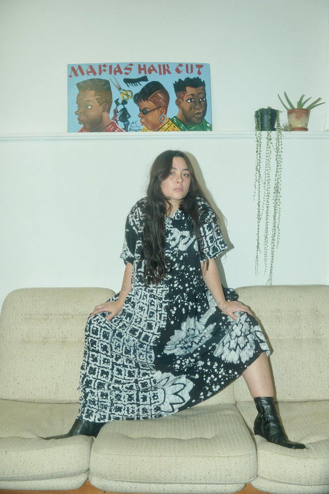 Stylish Imperium Dress in 2 Party System print, accessorized with black boots, in a cozy indoor setting with artistic decor.