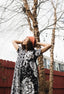 Chic Imperium Dress in monochrome floral, paired with a red hat, against a rustic red fence and bare tree backdrop.