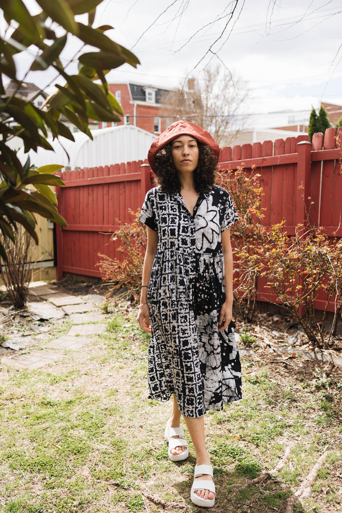 Imperium Dress in 2 Party System print, worn in a garden setting, featuring geometric and floral patterns with a relaxed fit.