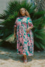 Imperium Dress in pink and green Pool Party print, outdoor setting with palm plant backdrop, capturing a tropical essence.