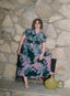 Imperium Dress in green and pink patterns, casual elegance on a stone fireplace against a textured stone wall backdrop.