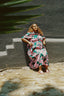 Imperium Dress in Pool Party print, seated against a dual-tone wall, with palm shadow play, embodying a serene vibe.
