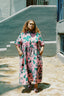 Imperium Dress in vibrant pink and turquoise, outdoor setting with grey wall and window, under bright sunlight.