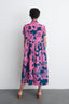 Imperium Dress in Pool Party print, gathering at waist, flowing hem, paired with peach heels, against a clean white wall.