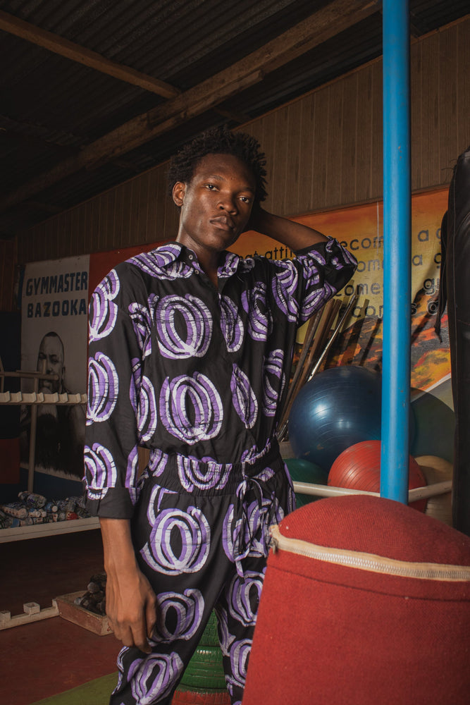 Kpong Trousers in Good Signal print, dark outfit, gym setting, promoting an active lifestyle, handcrafted in Ghana.
