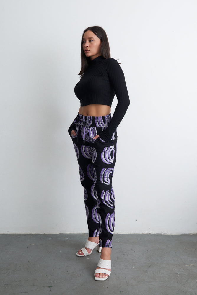 Kpong Trousers in Good Signal print, black with purple circles, cropped top, white heels, chic urban style.