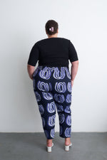 Back view of Kpong Trousers in Good Signal print, paired with sleek black top and light shoes, against a minimalist backdrop.