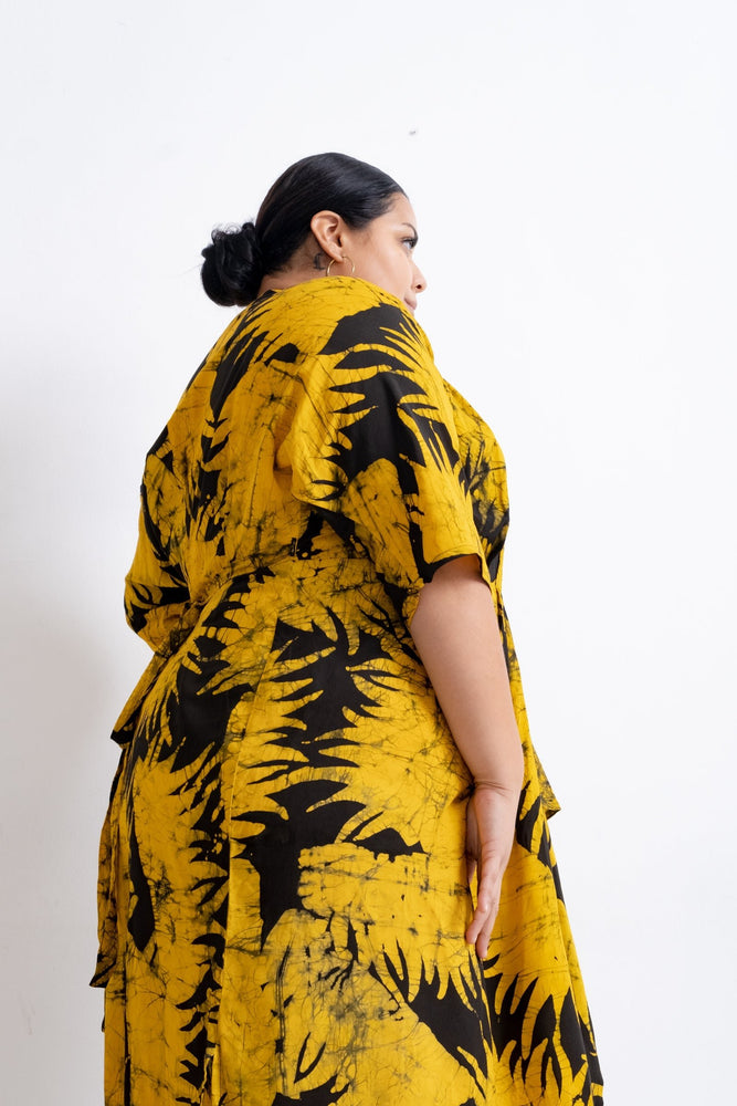 Model in yellow Letsa Dress with black leaf design, hair in bun, highlighting loose fit and flow against a white background.
