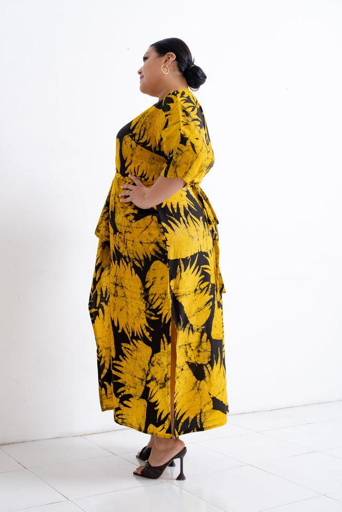 Side view of vibrant yellow Letsa Dress with black leaf patterns, model wears high-heeled shoes against a white background.