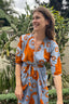 A woman wearing the Letsa Wrap dress in All Ideas, an orange and blue abstract flower hand-batiked print.