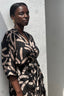 A woman in a wrap dress with a batik print, warm tan cantaloupe slice-like shapes scattered against a black background.