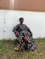 Woman in Letsa wrap dress with Cantaloop print, sitting on chair in front of wall.