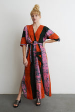 Colorful Letsa wrap dress in Carmine print, with wide sleeves and cinched waist, against a plain white wall.