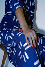 Seated Letsa Dress in Middle Path a blue with white print, red nail polish and bracelet, against a light-colored backdrop.