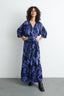 Woman in Letsa Rorschach wrap dress, highlighting V neckline and waist tie, against a plain backdrop.