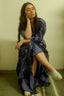 Person seated on metal chair in blue and black patterned Letsa dress against light green wall, white heeled shoes.
