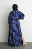 Long Letsa Rorschach dress with side slit and wide sleeves, paired with white wooden clog shoes.