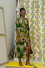 Model in Letsa dress against patterned backdrop, with green swirls complementing dress’s colorful design.