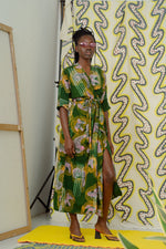 Model in Letsa dress against patterned backdrop, with green swirls complementing dress’s colorful design.