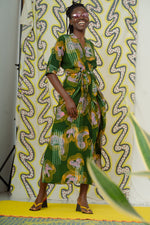 Model in Letsa dress against yellow patterned backdrop, highlighting green, pink and white print and black heels.