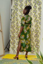 Back view of a model in Letsa dress against vibrant patterned backdrop, with red heels on yellow mat.