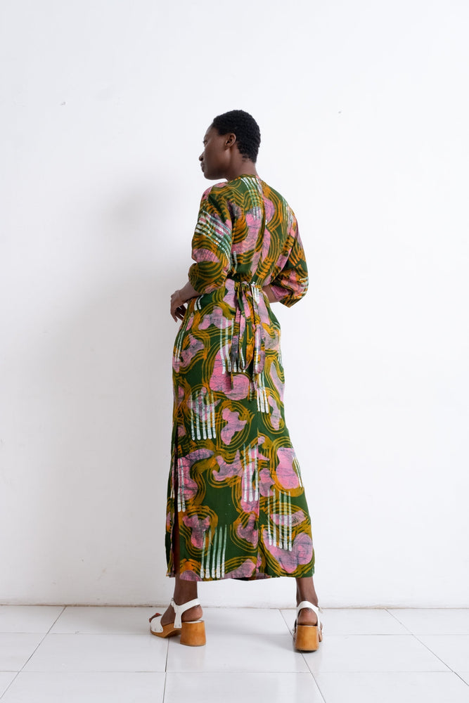 Woman in vibrant Letsa Dress with abstract green, pink & yellow patterns, ankle-length, white sandals.