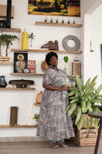 Nonna Dress in Snakebite pattern, chic indoor vibe with wooden crate and green plant, perfect for a cozy atmosphere.