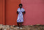 Person in Sampa Dress against red wall, showcasing the dress’s white and purple print and casual white sandals.