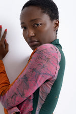 Side view of person in Stricta Turtleneck, pink, orange and green marbled design, against white wall.