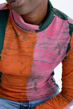 Close up of the vibrant Stricta Turtleneck in Carmine print, textured orange, pink, green pattern, casual denim hint.