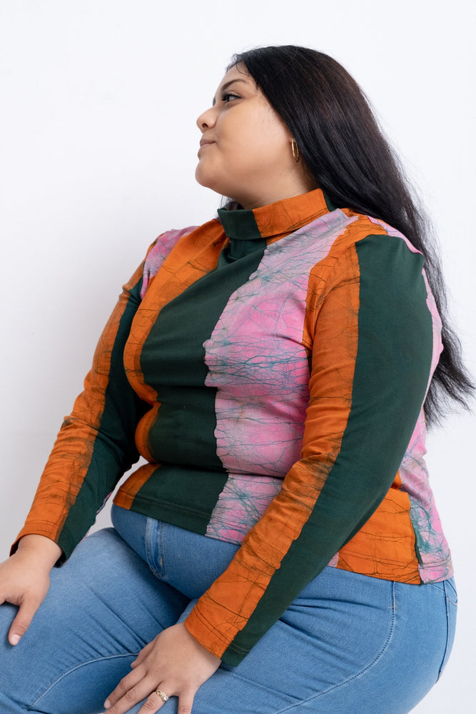 Multicolored Stricta Turtleneck in Carmine, paired with blue jeans, seated sideways, long black hair, white background.
