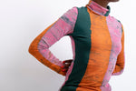 Confident stance in Stricta Turtleneck, color-block design with pink, orange, green, crackled texture no head shown.