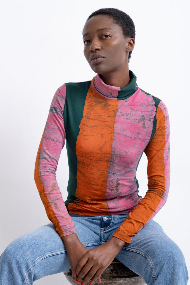 Fitted Stricta Turtleneck in bold Carmine print, deep pink and green stripes, paired with blue jeans, relaxed posture.