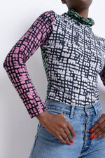Fashionable Stricta Turtleneck with pink and white shapes on black, high-necked and long-sleeved, paired with jeans.