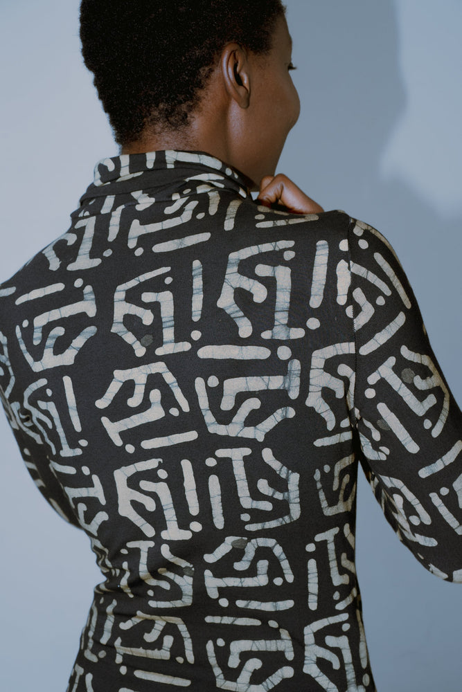 Person wearing the Stricta Turtleneck with the unique Chale print of gold lines and shapes against a dark background.