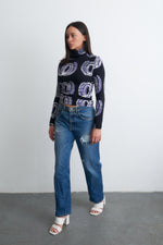 Person in stylish attire featuring the Stricta Turtleneck in Good Signal with its unique pattern, paired with denim jeans.