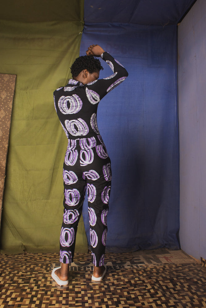 Back view of the Stricta Turtleneck in Good Signal, model stands with her hands above her head against colorful fabrics.
