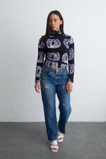 Person in a casual yet stylish outfit, the Stricta Turtleneck in Good Signal with its unique patterns, paired with jeans