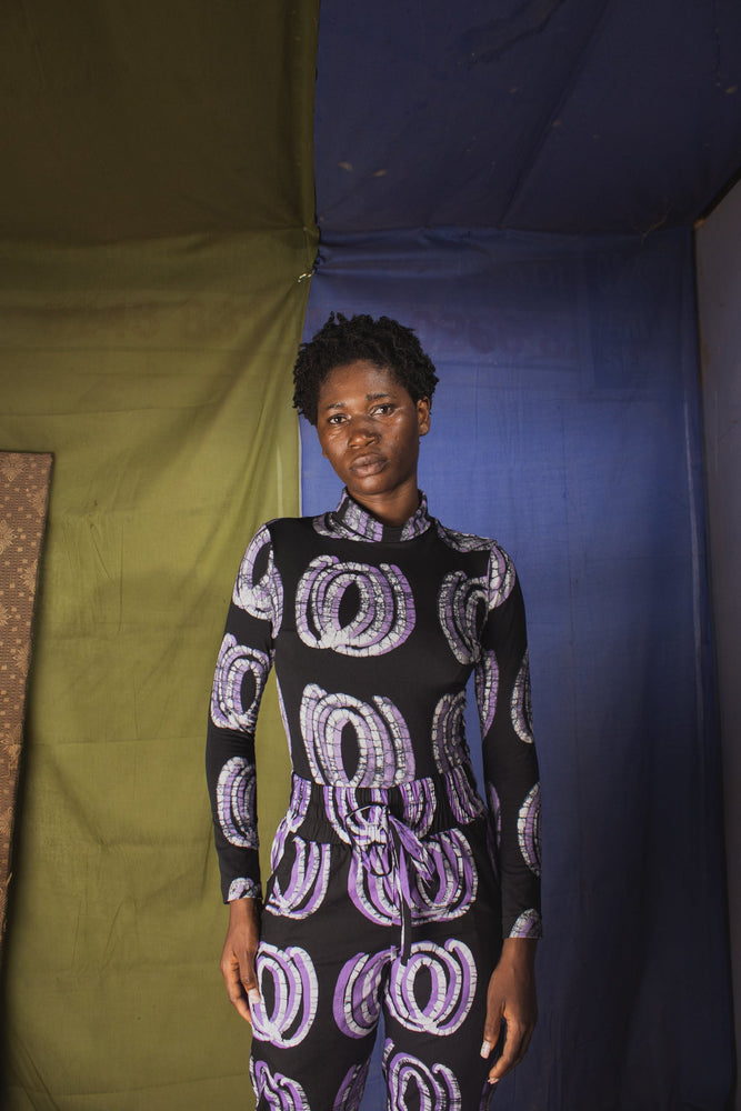 Model in the Stricta Turtleneck in Good Signal with a unique circular print, standing against a backdrop of vibrant fabrics.