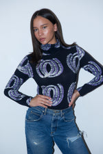 Woman in the Stricta Turtleneck in Good Signal, a cozy, stretchy, hand-batiked top, paired with jeans for a stylish look.