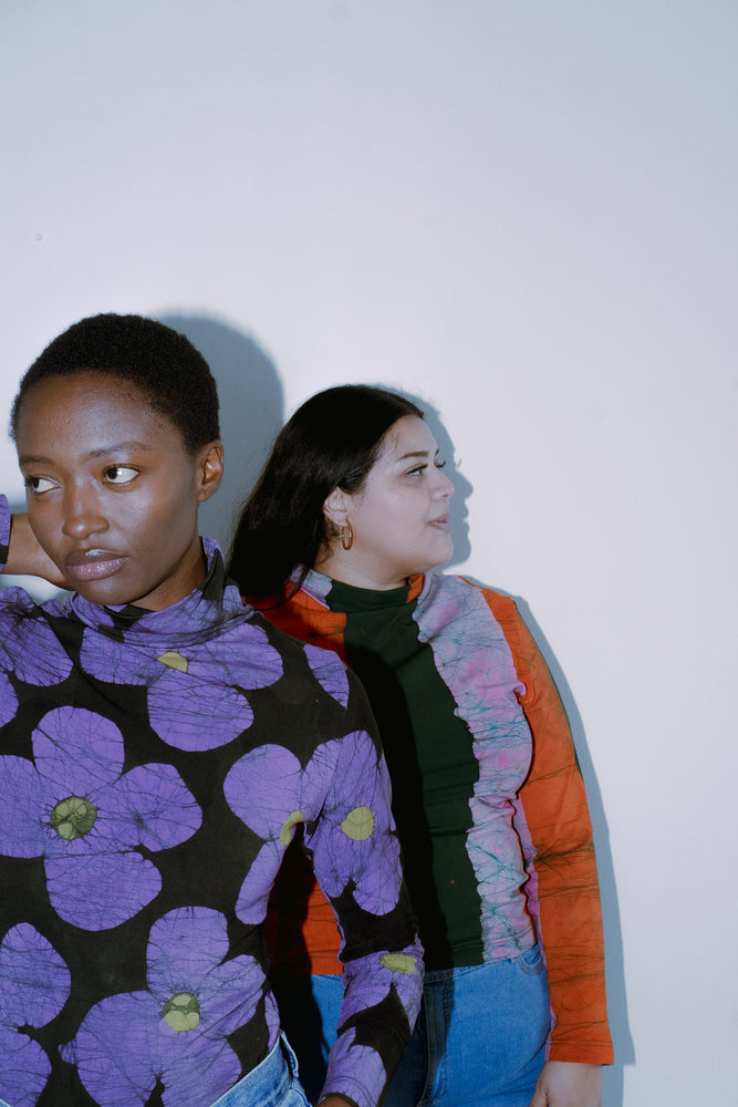 Two people standing side by side in vibrant, patterned clothing, featuring the Stricta Turtleneck in Love Perfect print.