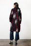 Rear view of long striped Theca Coat with red, black, and white pattern, paired with jeans and black boots.