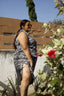 A person in a zebra print shirtdress standing beside a flowering plant, showcasing the dress's side slit.