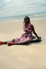 A woman lounging on the sandy beach in the Tropicana dress, a flattering and comfortable dress with timeless details.